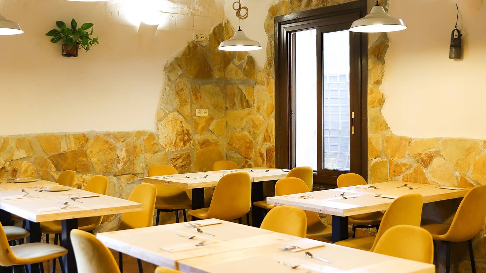 Interior de El Olivo con pared de piedra, mesas preparadas y luz calida